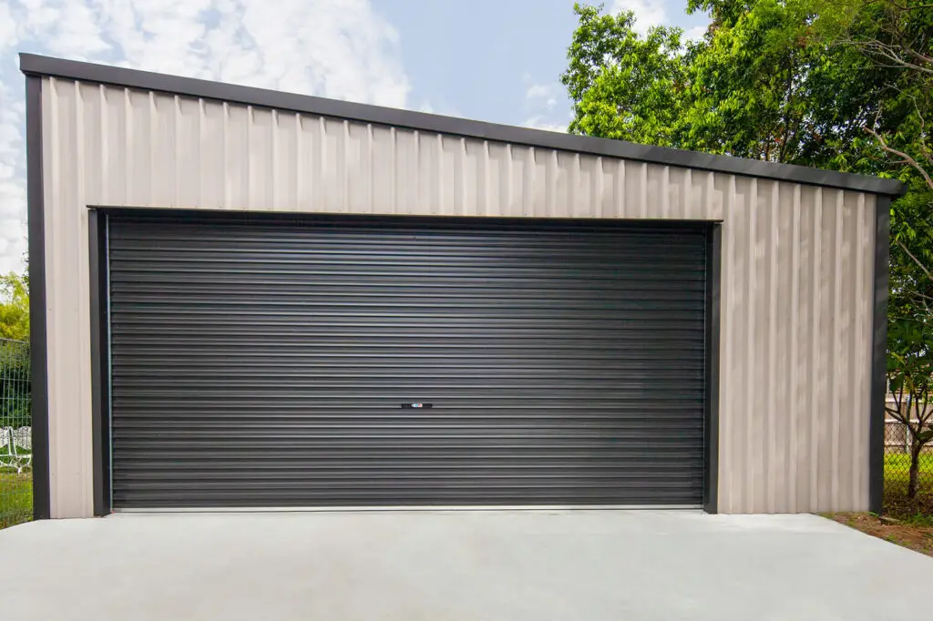 Close-up front view of a modern backyard garage in Mitchelton, showcasing the skillion roof apex, COLORBOND® cladding, and surrounding trees and fencing.
