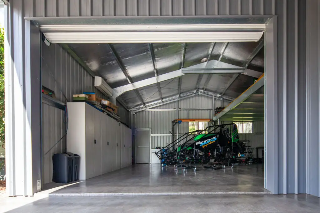 Inside view of the garaport leading into a sprint car workshop shed, featuring roof insulation, a whirlybird, mezzanine storage, and an air-conditioned workspace.