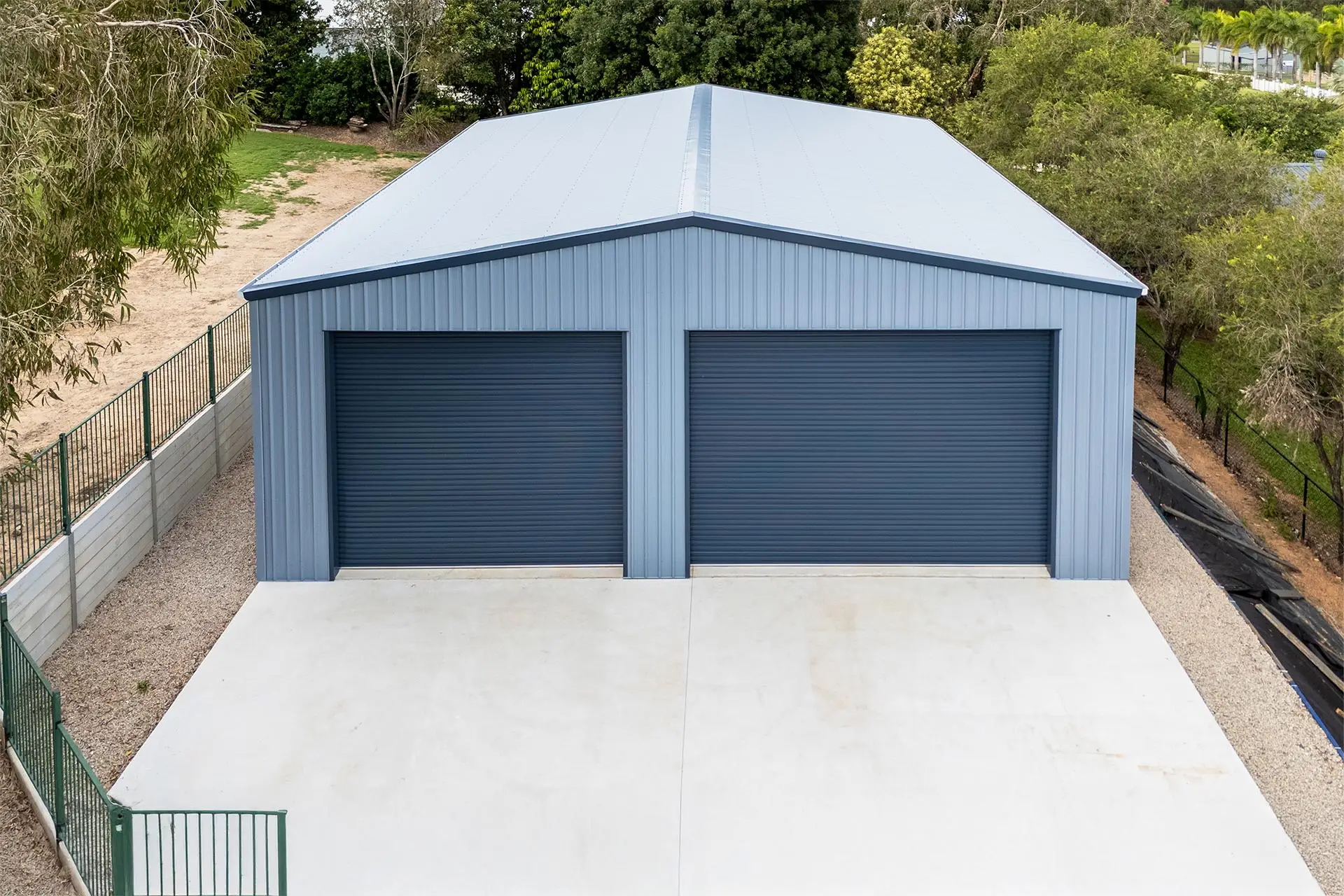 Drone view of a caravan and boat storage shed surrounded by native trees with visible retaining wall and driveway.