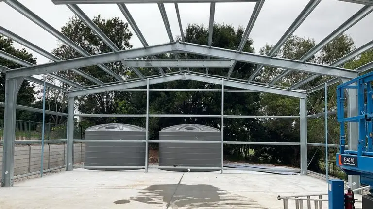 Steel shed frame installed with twin water tanks behind caravan and boat storage shed.