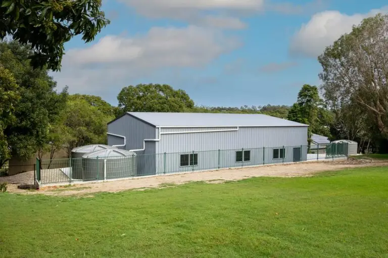 Side view of a caravan and boat storage shed with water tanks, green fencing, and multiple windows.